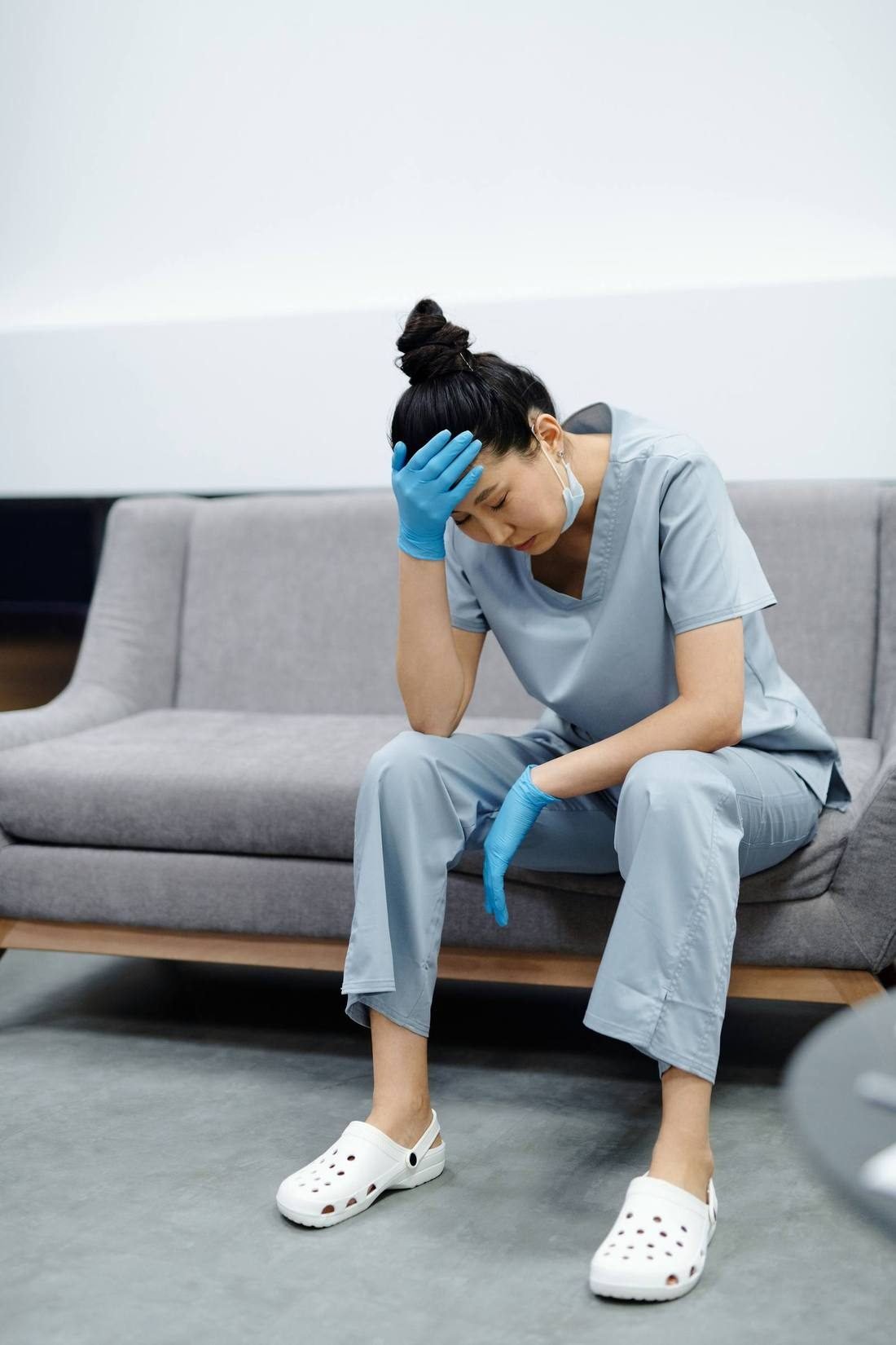 A nurse sitting with her head in her hand, worn down after a shift