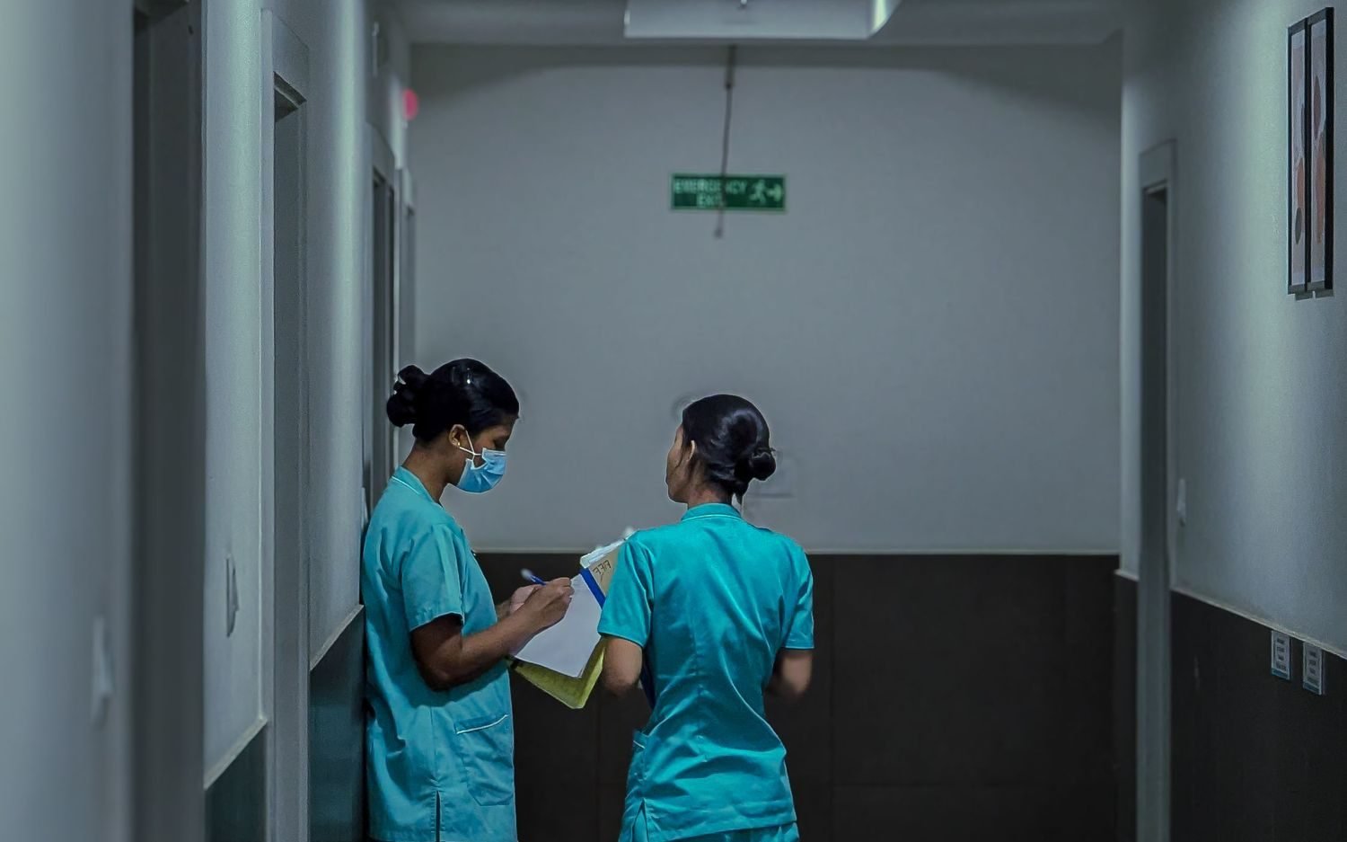 Two nurses conferring in a dimly lit hospital corridor