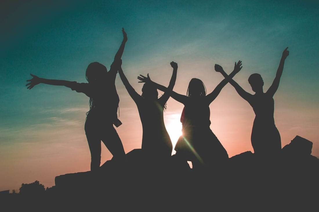 Silhouettes of women with their arms raised against an evening sky